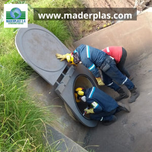 Operarios instalando una charnela o válvula antirretorno de polipropileno Maderplast en un canal de drenaje para evitar el reflujo de aguas en un sistema de alcantarillado.