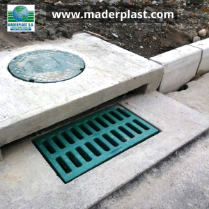 Rejilla plástica de polipropileno Maderplast instalada en un sumidero para drenaje de aguas lluvias junto a una tapa de pozo de inspección en una obra de infraestructura vial.