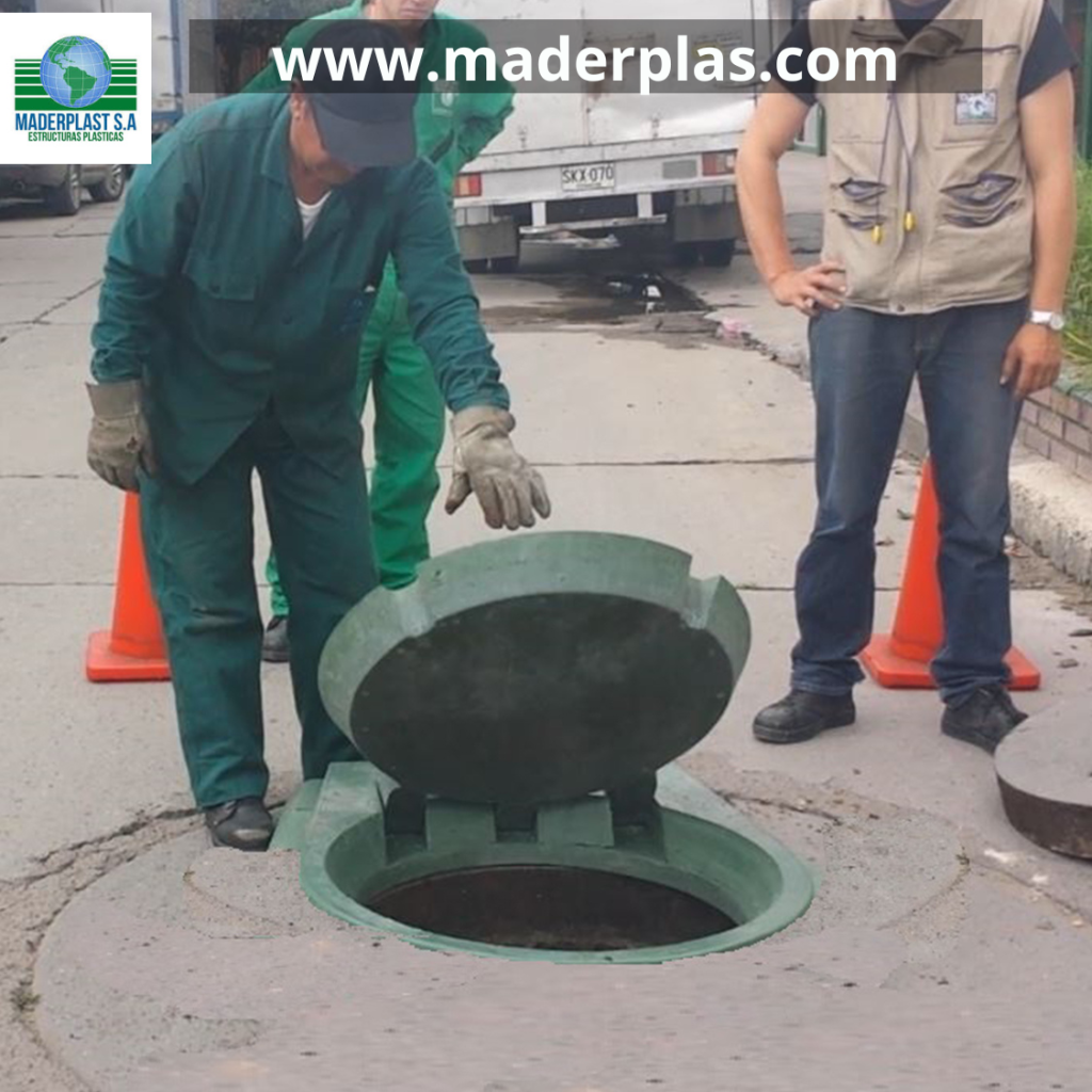 Tapa plástica para pozo de inspección instalada en vía pública con sistema de bisagra, abierta para facilitar labores de inspección y mantenimiento en redes de alcantarillado y servicios públicos.