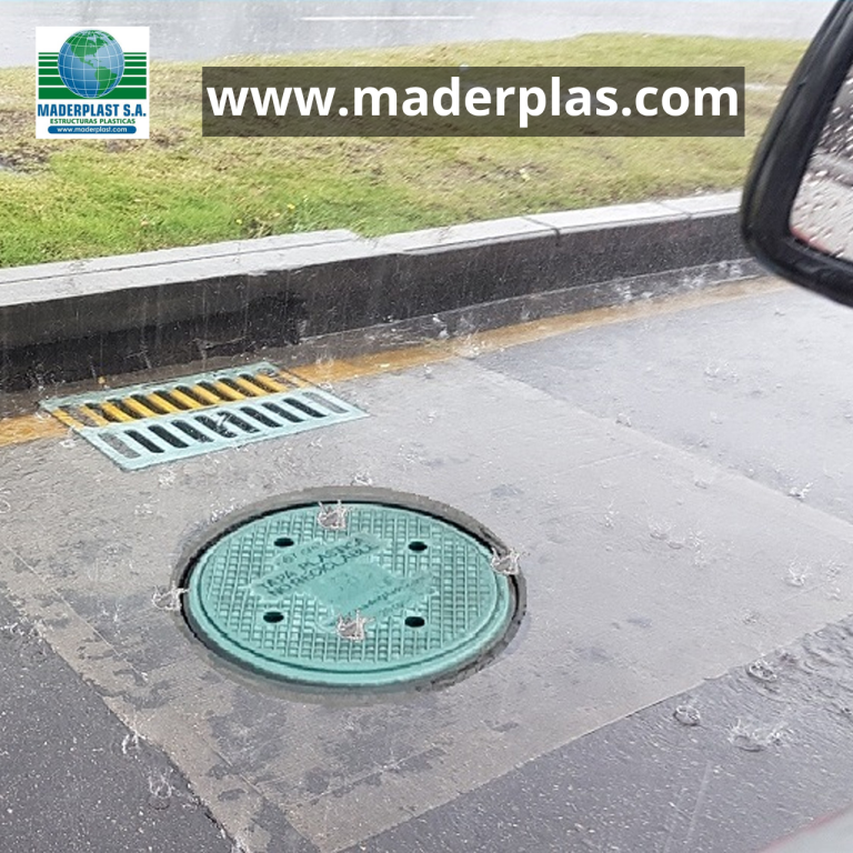 Tapa de alcantarilla plástica Maderplast instalada en un pozo de inspección sobre una vía urbana durante lluvia, fabricada en polipropileno de alta resistencia para redes de alcantarillado.