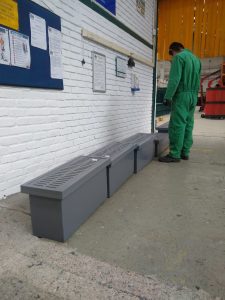 Cárcamo plástico prefabricado con rejilla instalada en área industrial, inspeccionado por trabajador en uniforme verde.