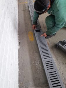Persona instalando una rejilla plástica de drenaje en piso de concreto junto a una pared blanca