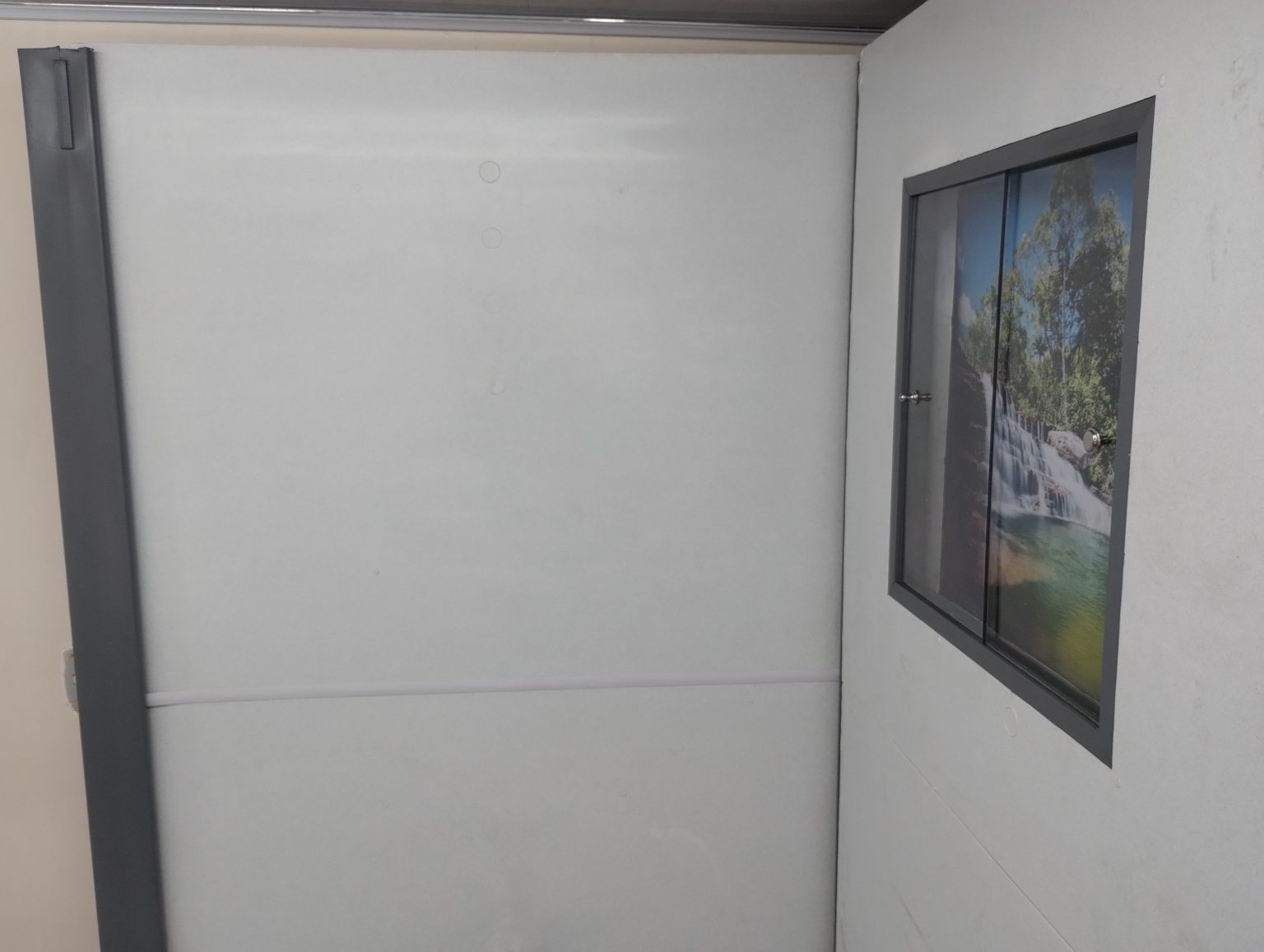 Vista en ángulo del módulo de pared y piso para campamento en polipropileno Maderplast, acabado blanco liso y panel decorativo con paisaje natural, diseño modular de alta resistencia y fácil limpieza.