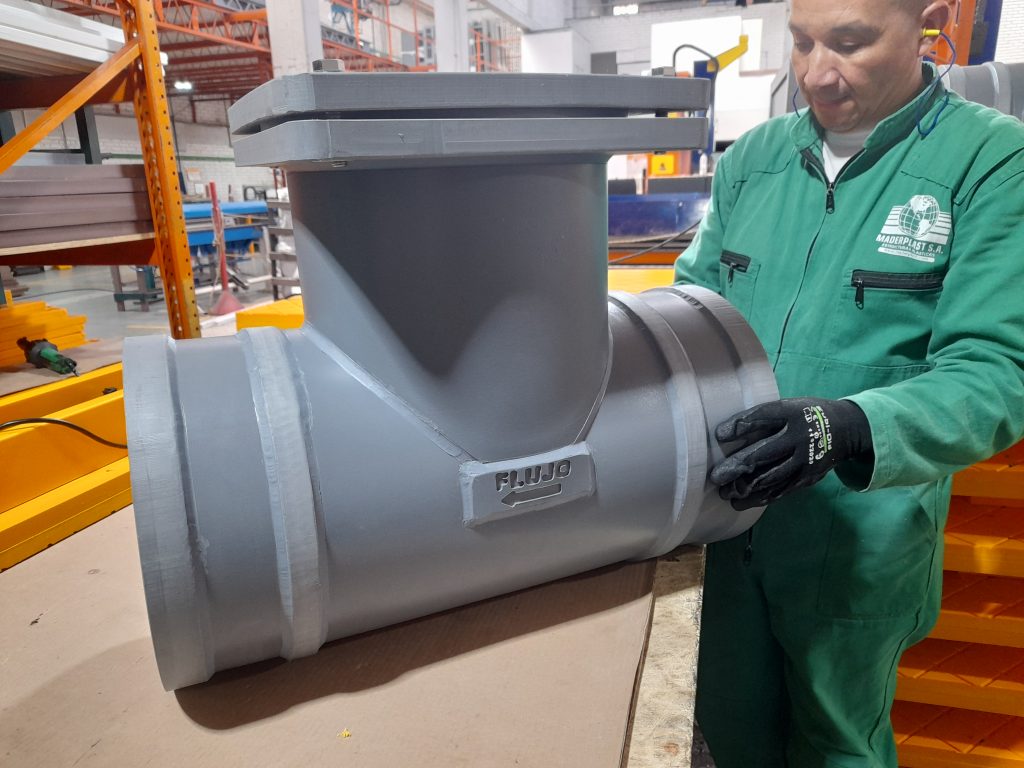 Operario sostiene válvula antirretorno plástica en polipropileno gris de gran tamaño, fabricada por Maderplast para sistemas de alcantarillado y drenaje.