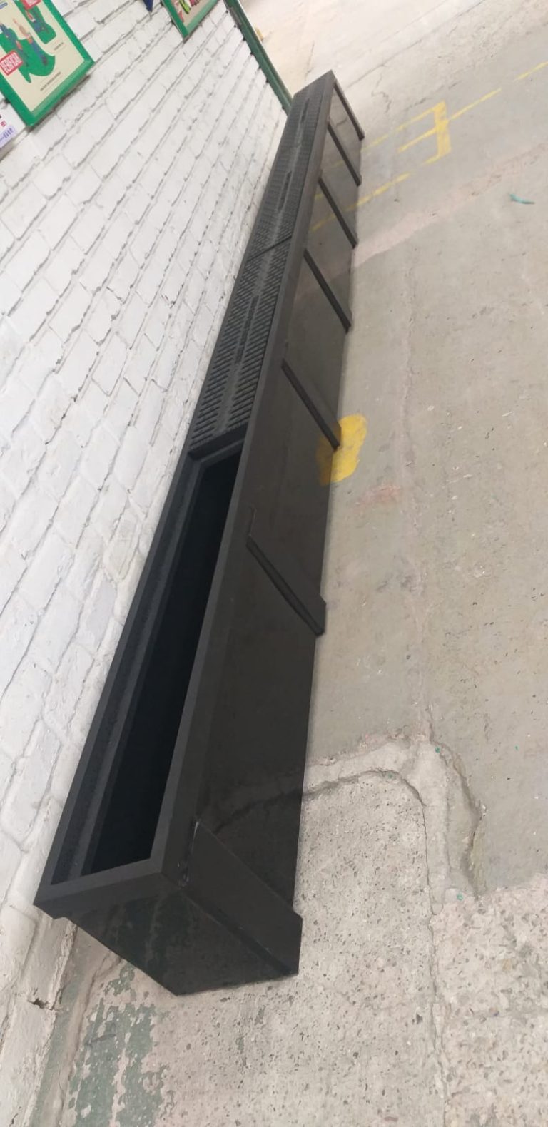 Canaleta prefabricada en polipropileno instalada en área industrial junto a una pared de ladrillo pintada de blanco.